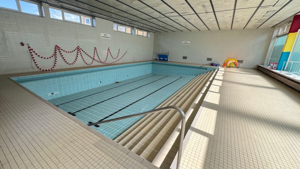 Blick über das leere Lehrschwimmbecken in der Lerchenschule Faßberg mit Treppeneinstieg, Handlauf und gefliestem Beckenumgang